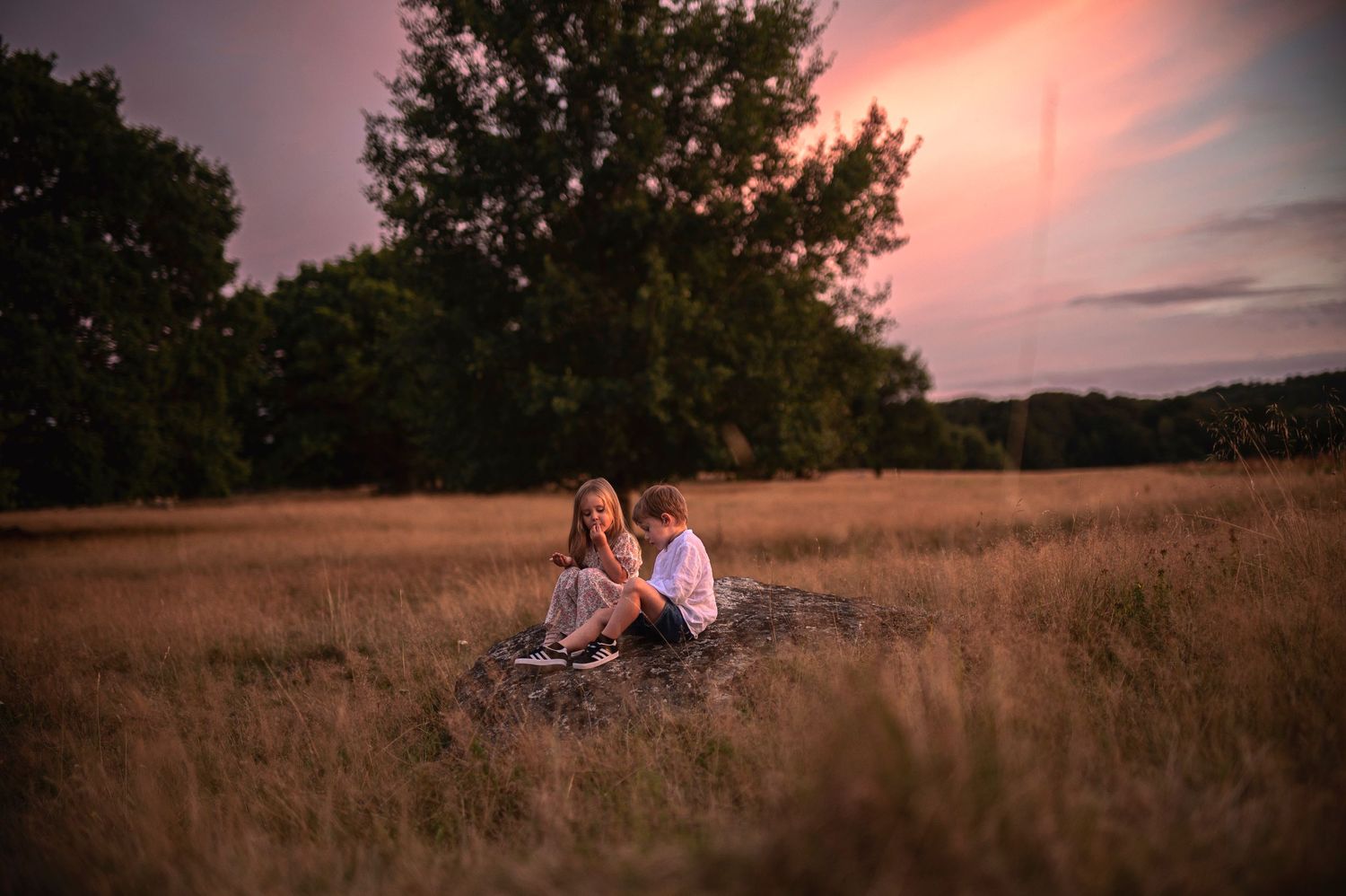 Two people sitting on blanket in golden field at sunset.