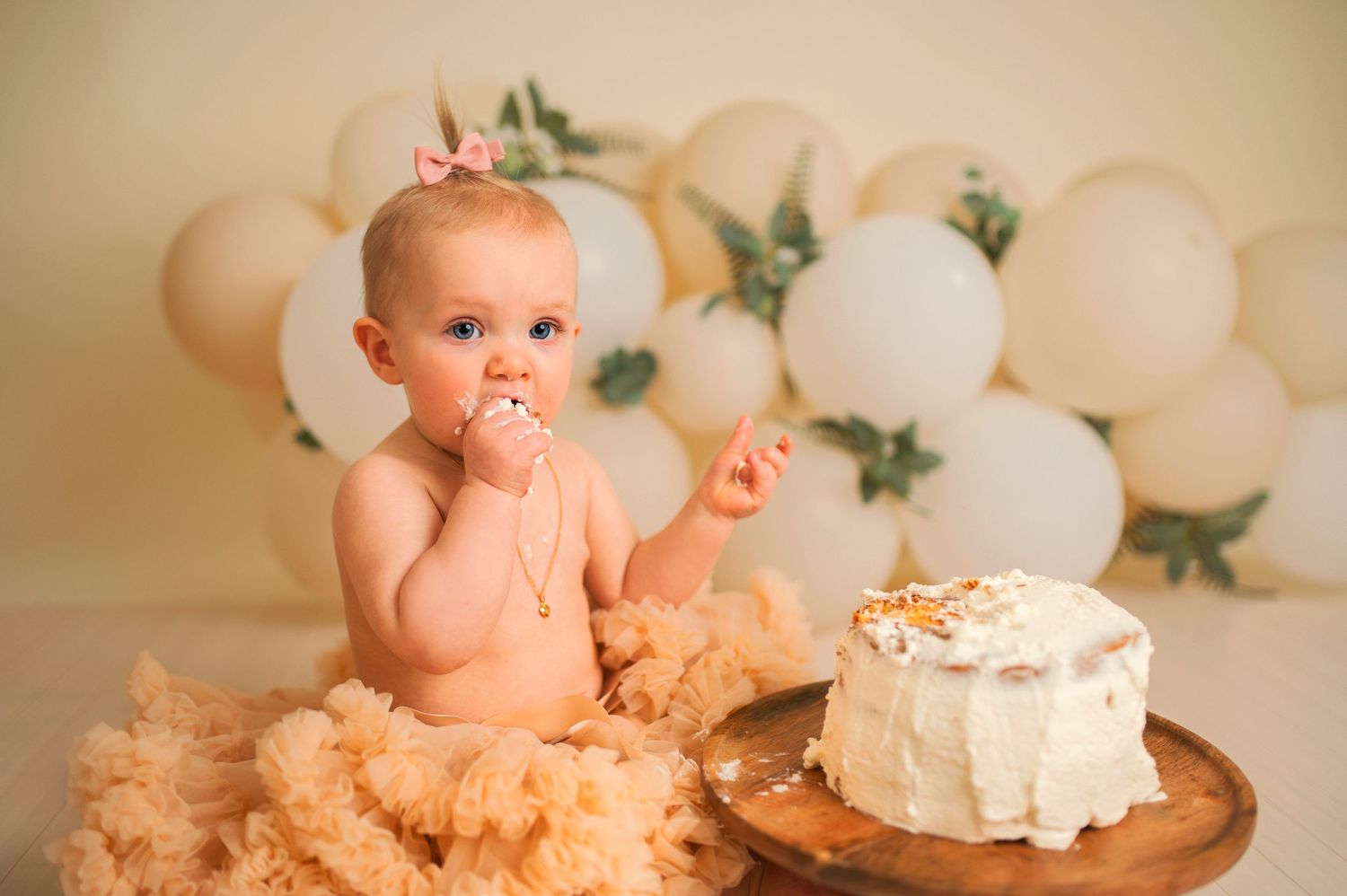 Cake smash photography session with white balloons and floral accents in the background.