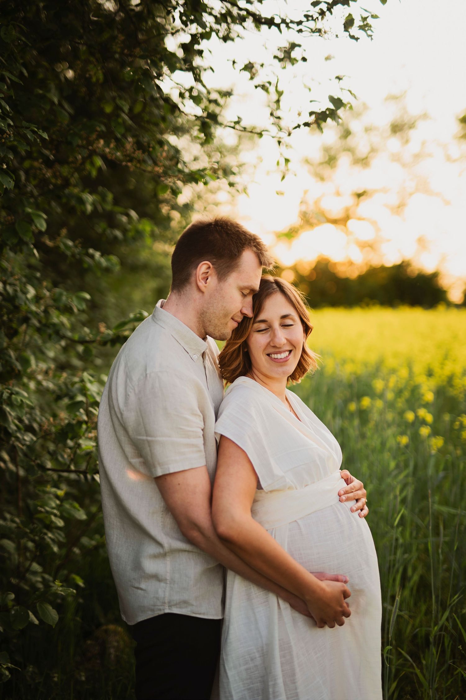 Intimate maternity moment captured in flowering field at golden hour.