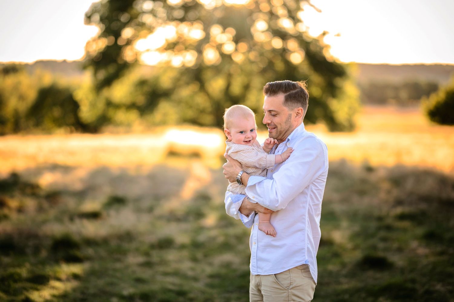 Parent holding baby against sunset backdrop in outdoor natural setting.