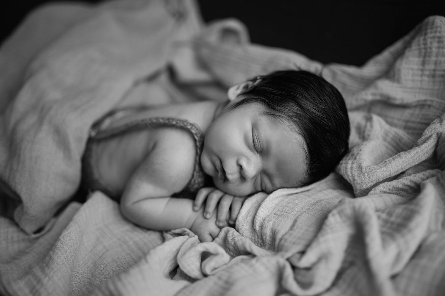 Peaceful newborn sleeping on soft fabric in black and white portrait.