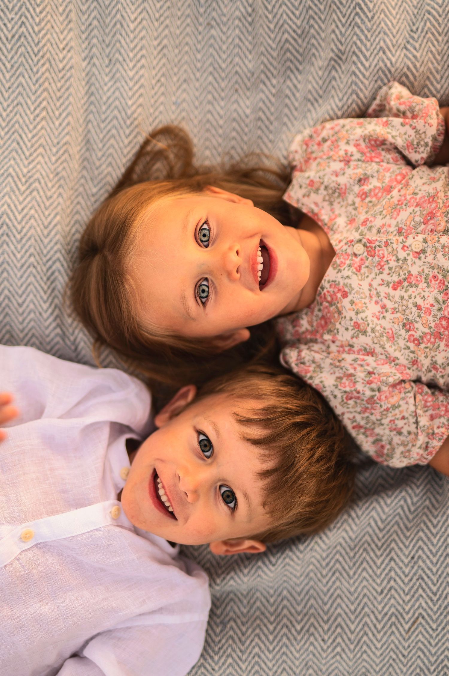 Two young children lying on patterned fabric smiling at camera.