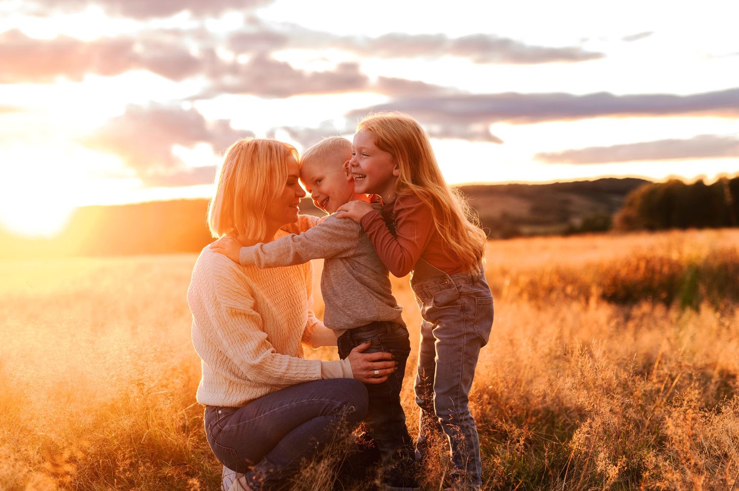 Joyful family cuddles together in a sun-kissed field during golden hour.