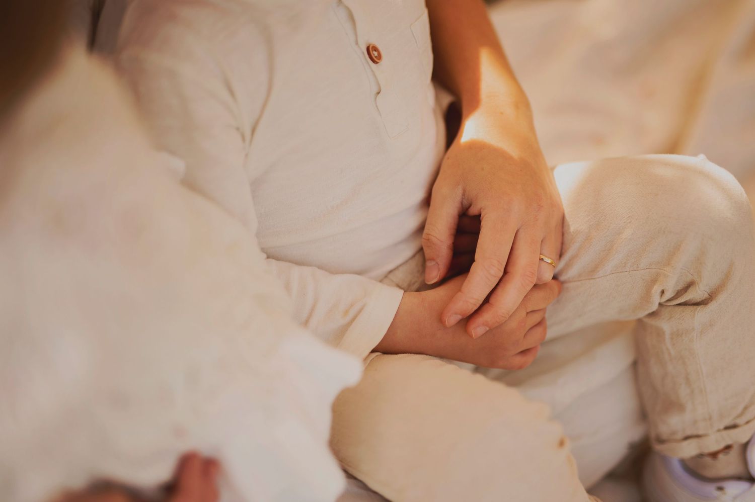 A pair of hands clasped together while sitting on a white blanket in warm lighting.