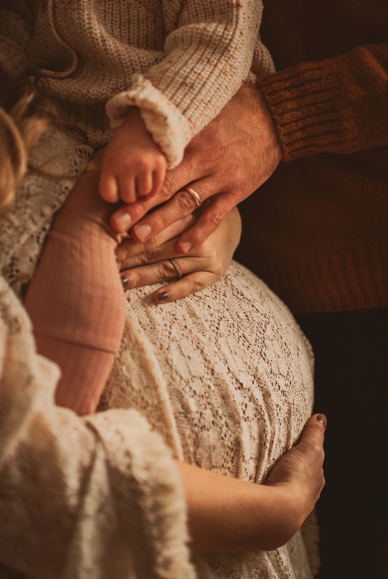 Delicate close-up of hands resting on lace dress in warm, moody lighting.