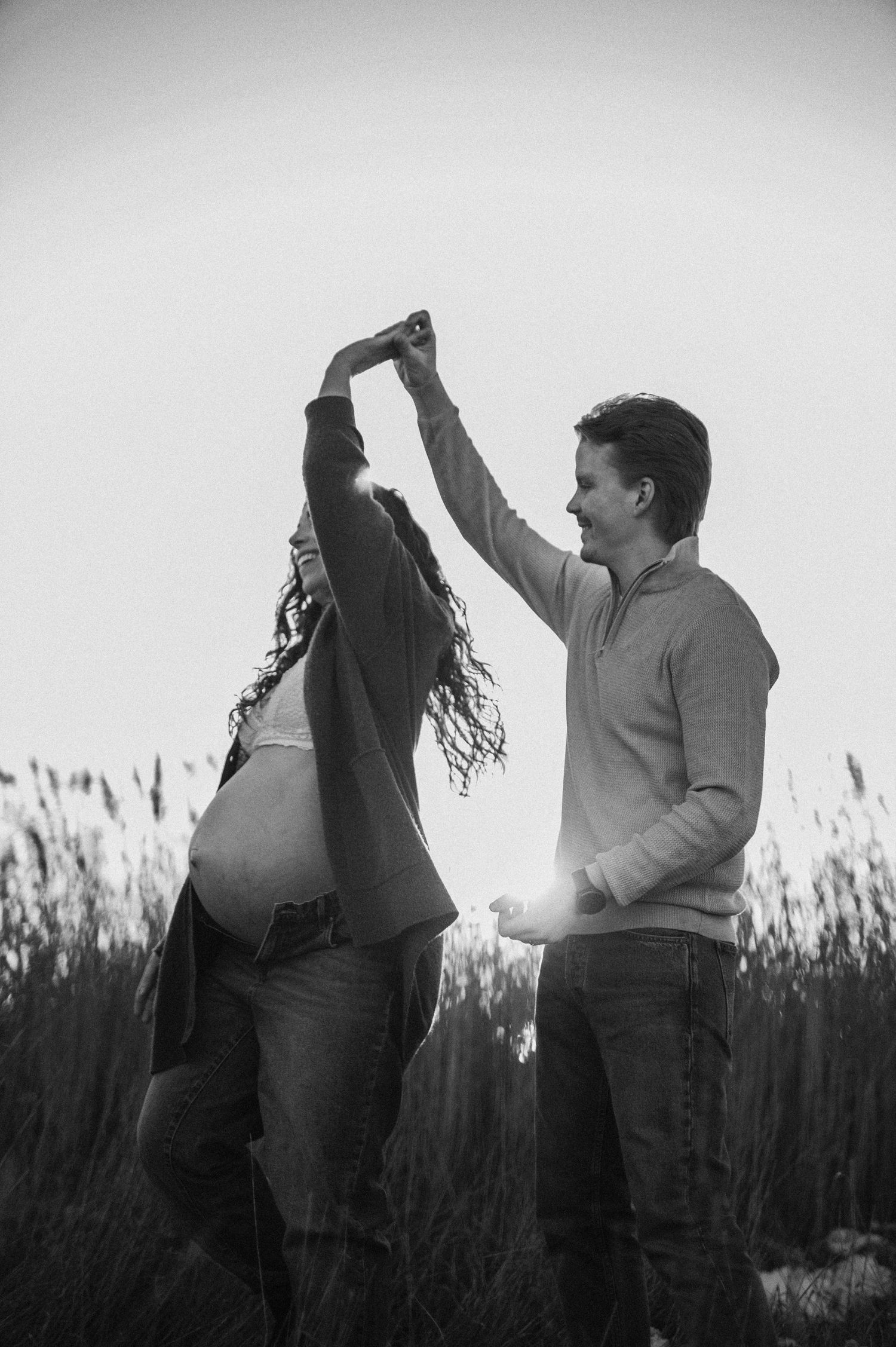 Black and white photo of couple dancing in field during maternity session.