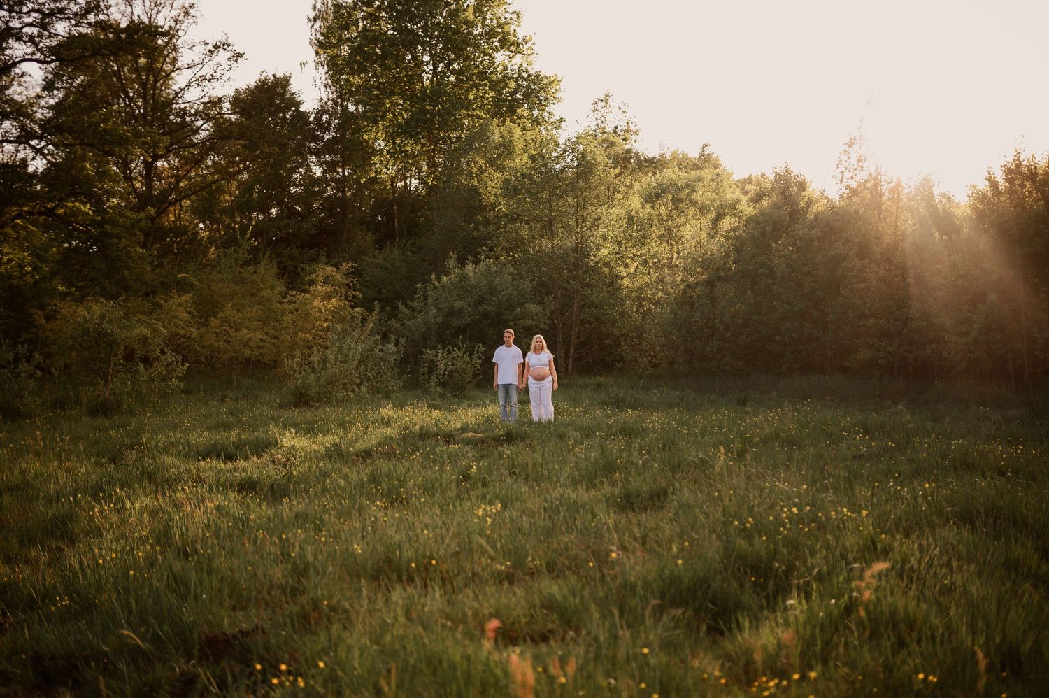 Distant view of couple standing together in a wildflower meadow during sunset.