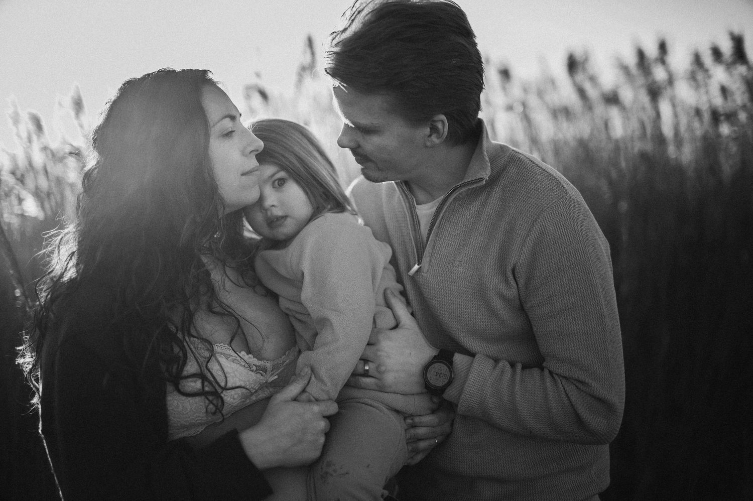 Svartvitt familjeögonblick i kvällsljus – fångat i högt gräs under golden hour i Skåne nära Hässleholm.