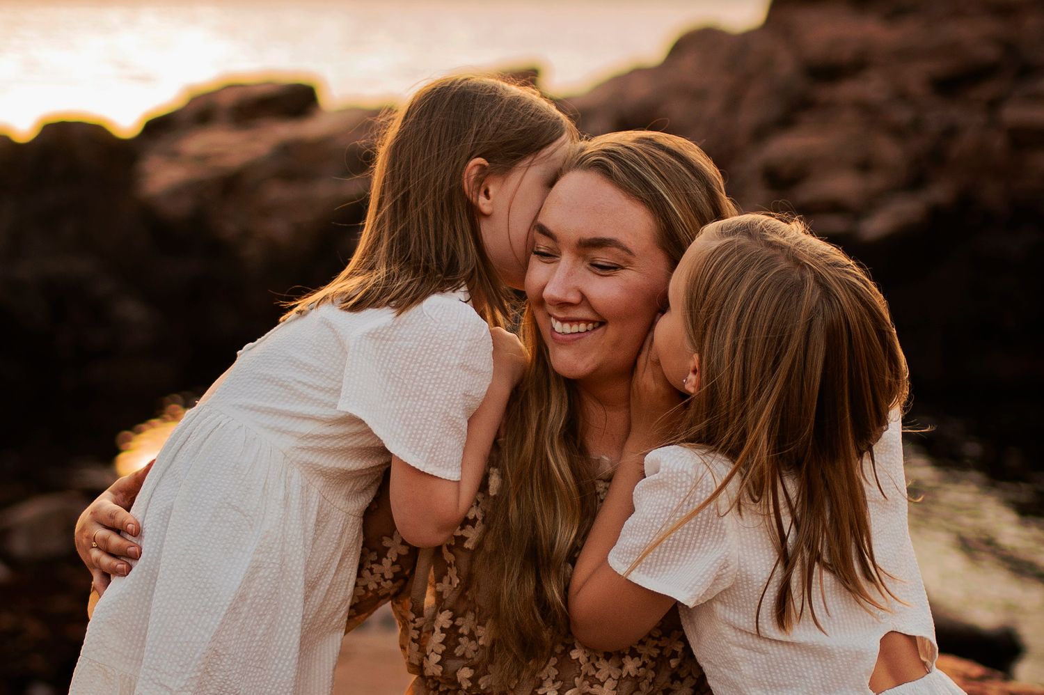 Joyful family moment captured on rocky coast during golden hour sunset.