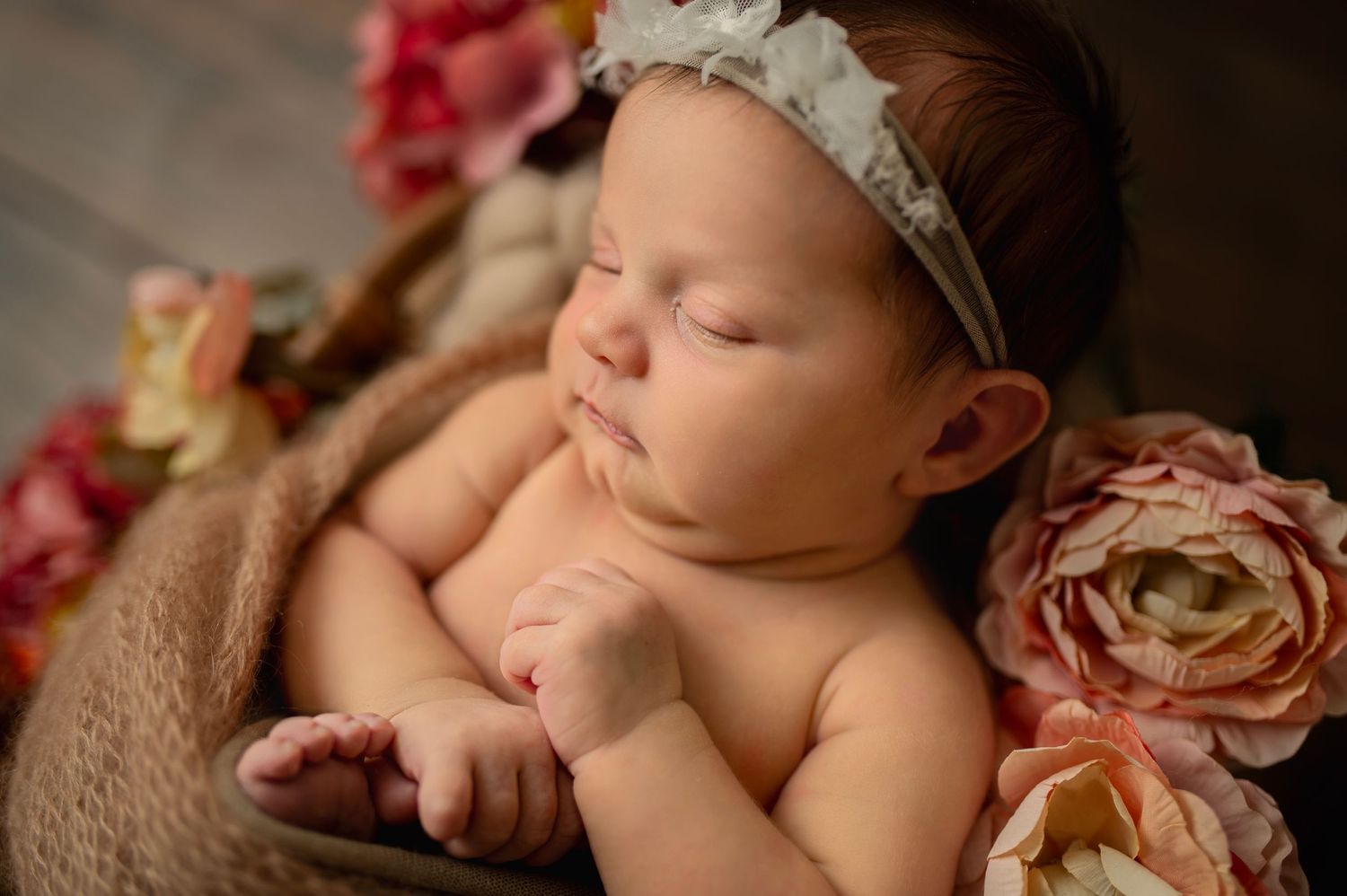 Sleeping baby with lace headband surrounded by pink and peach roses.