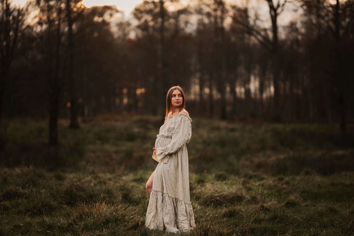 Woman in flowing white dress poses in misty field at dusk.