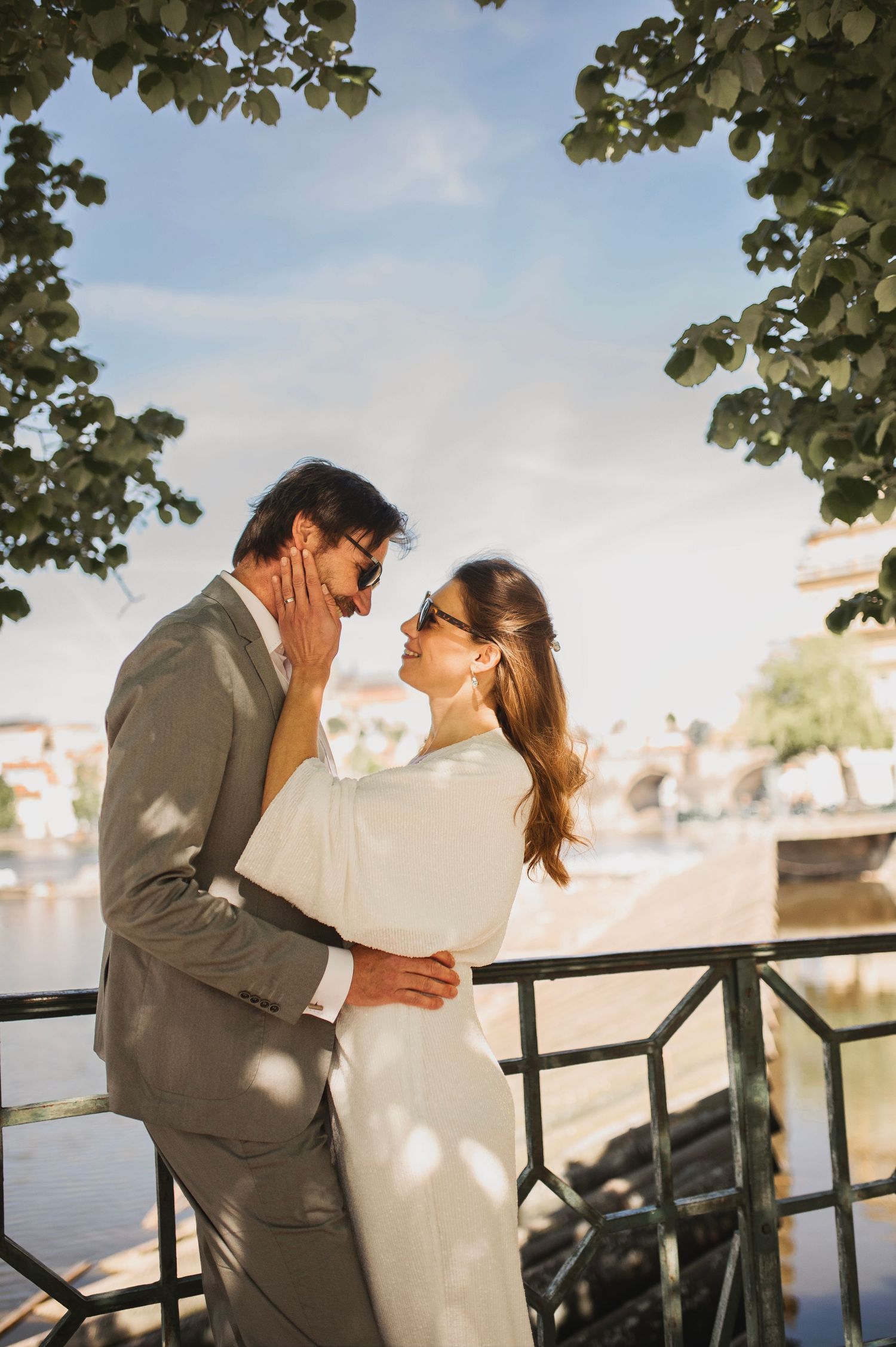 Couple shares joyful moment on balcony with dappled sunlight through leaves.