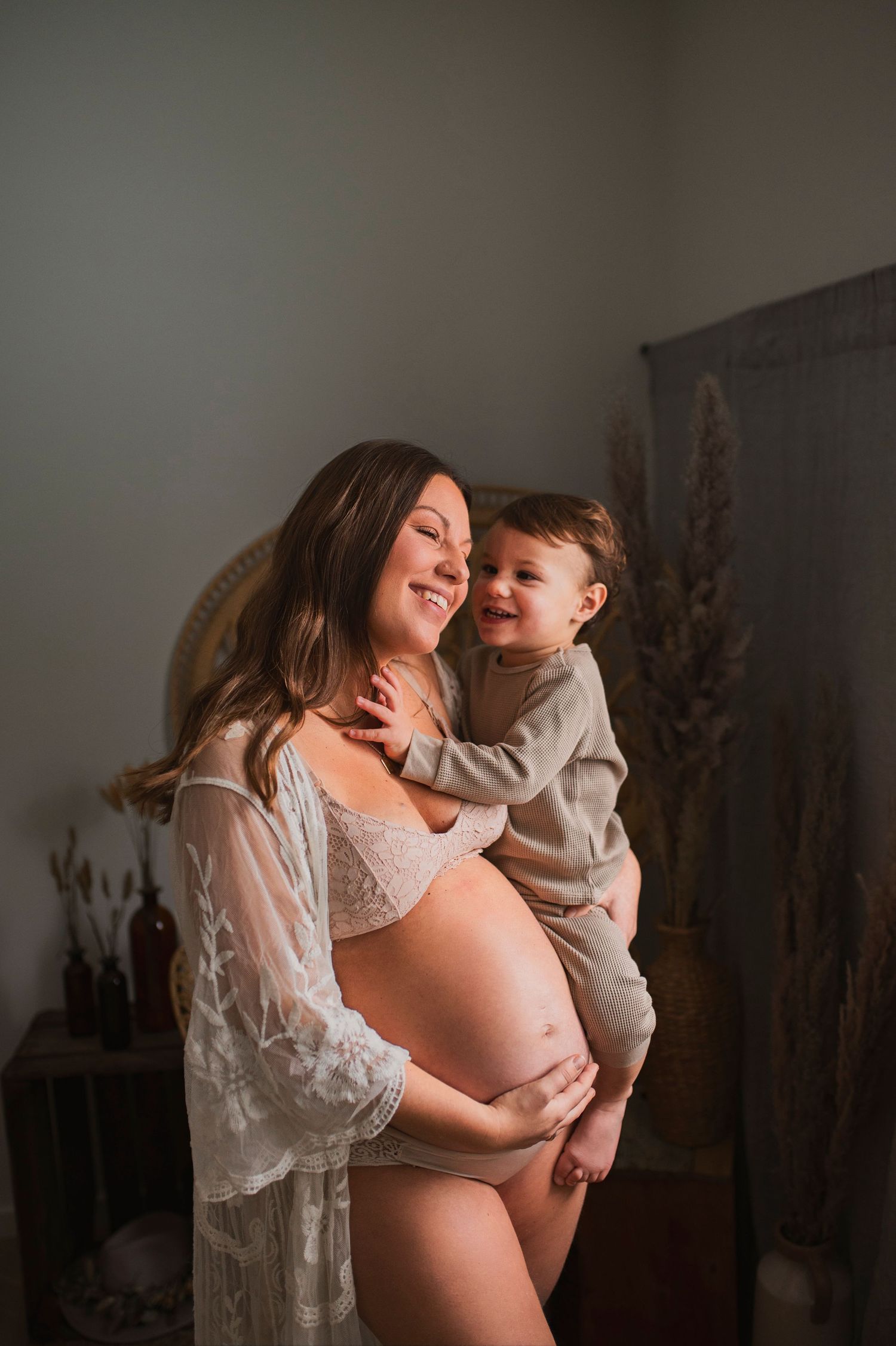 Candid maternity moment captured indoors with natural lighting and bohemian decor elements.