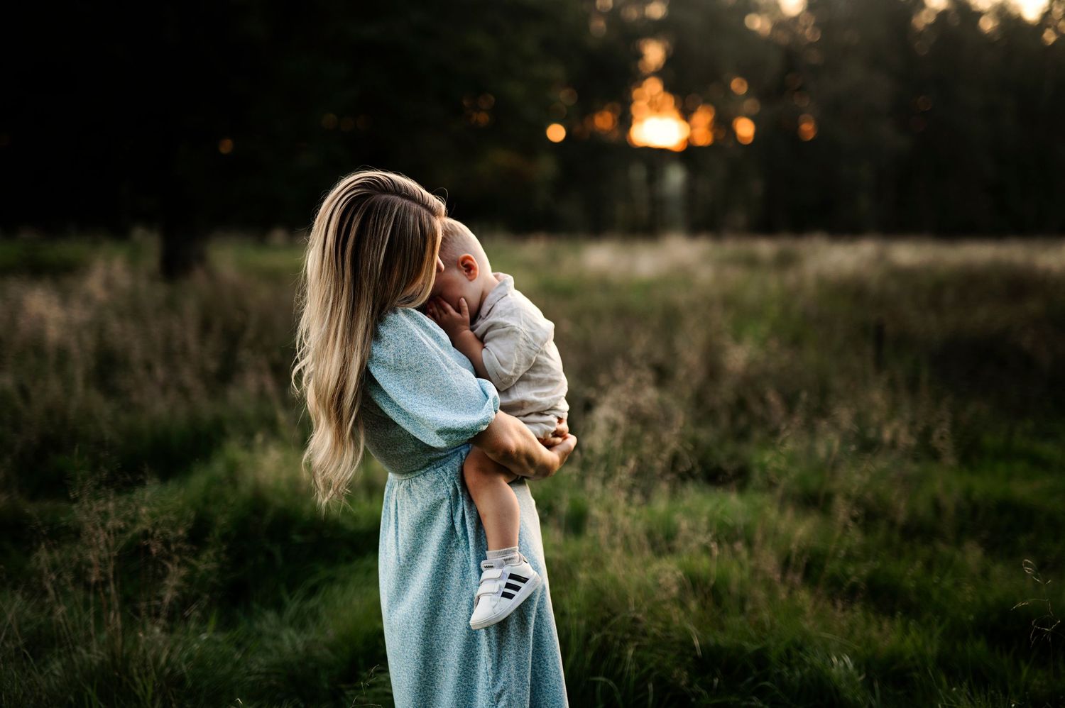 A tender moment captured in a field at sunset with trees silhouetted in the background.