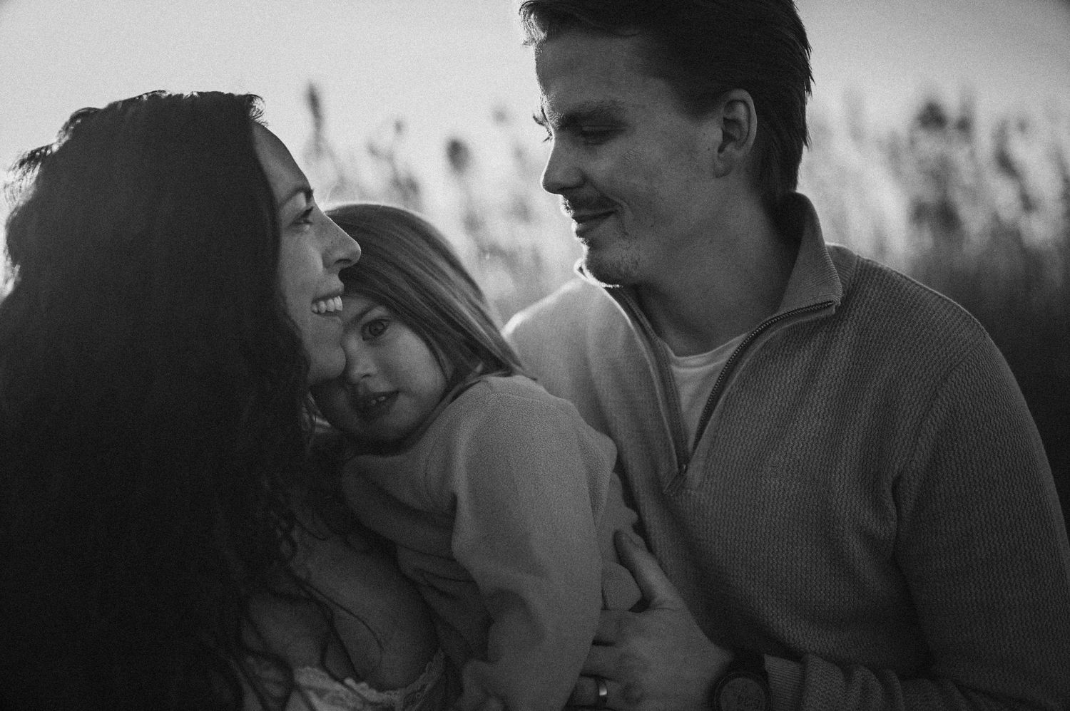Family sharing intimate moment together in black and white portrait with tall grass background.