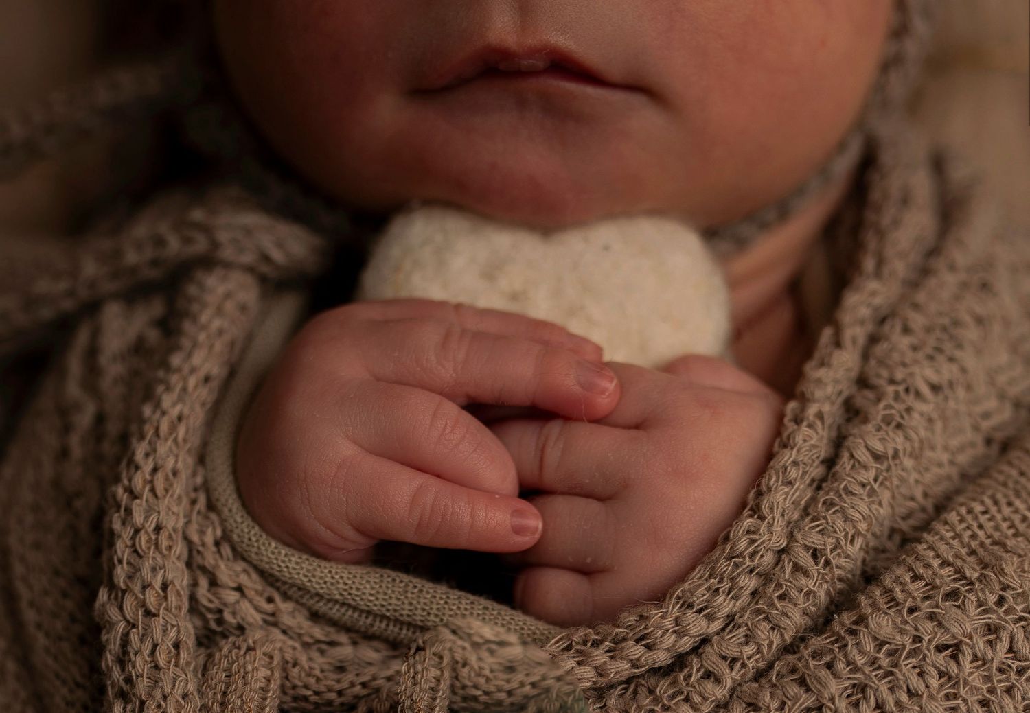 Close-up detail of tiny baby hands clutching soft fabric.