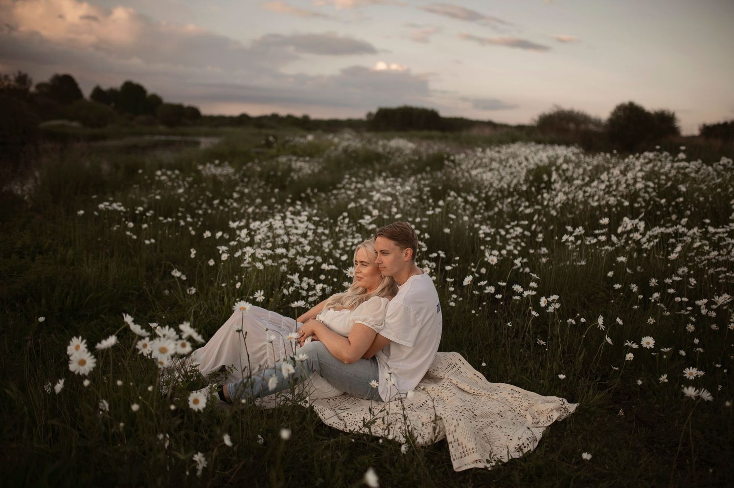Artistic sunset maternity portraits taken in a flowering meadow with soft natural lighting.
