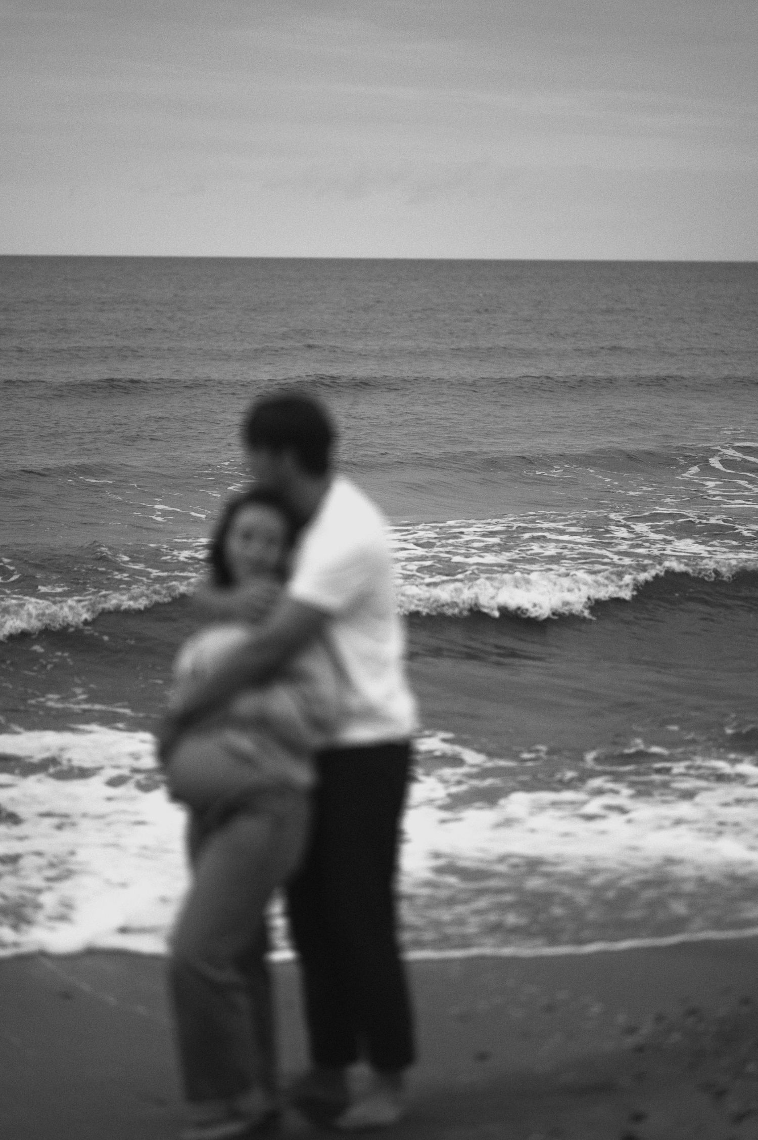 A blurred black and white photo of a couple embracing on the beach.