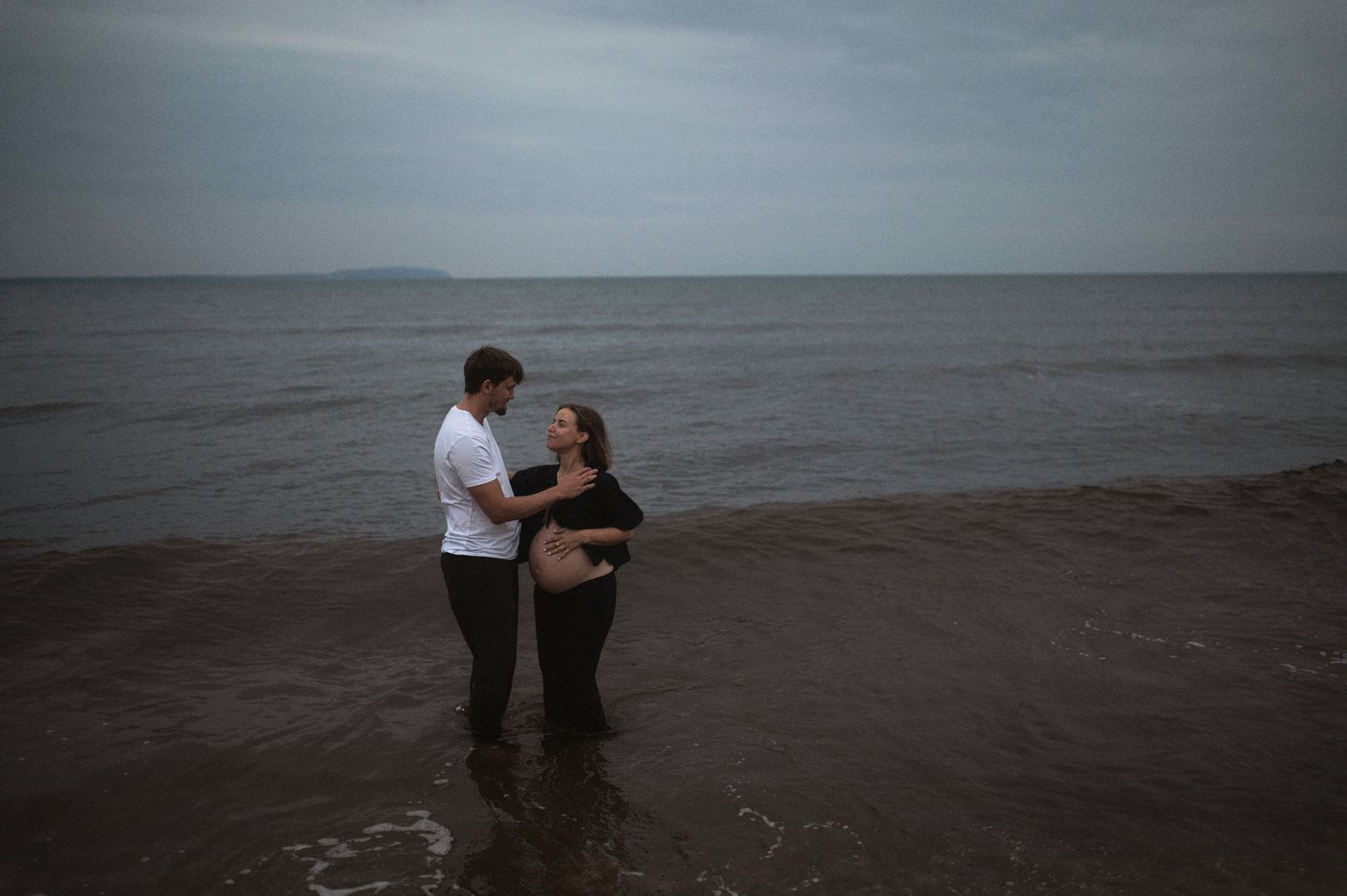 Couple embracing in ocean water during moody overcast weather.