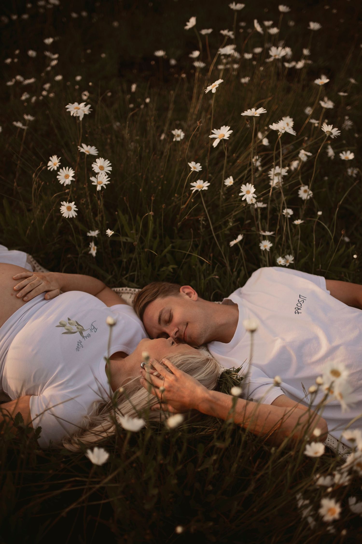 People lying in a dreamy meadow surrounded by delicate white daisies at dusk, dressed in white clothing.
