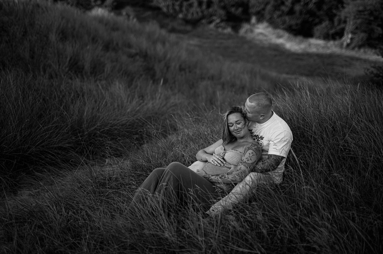 Romantic couple laying in tall grass during an outdoor photoshoot.