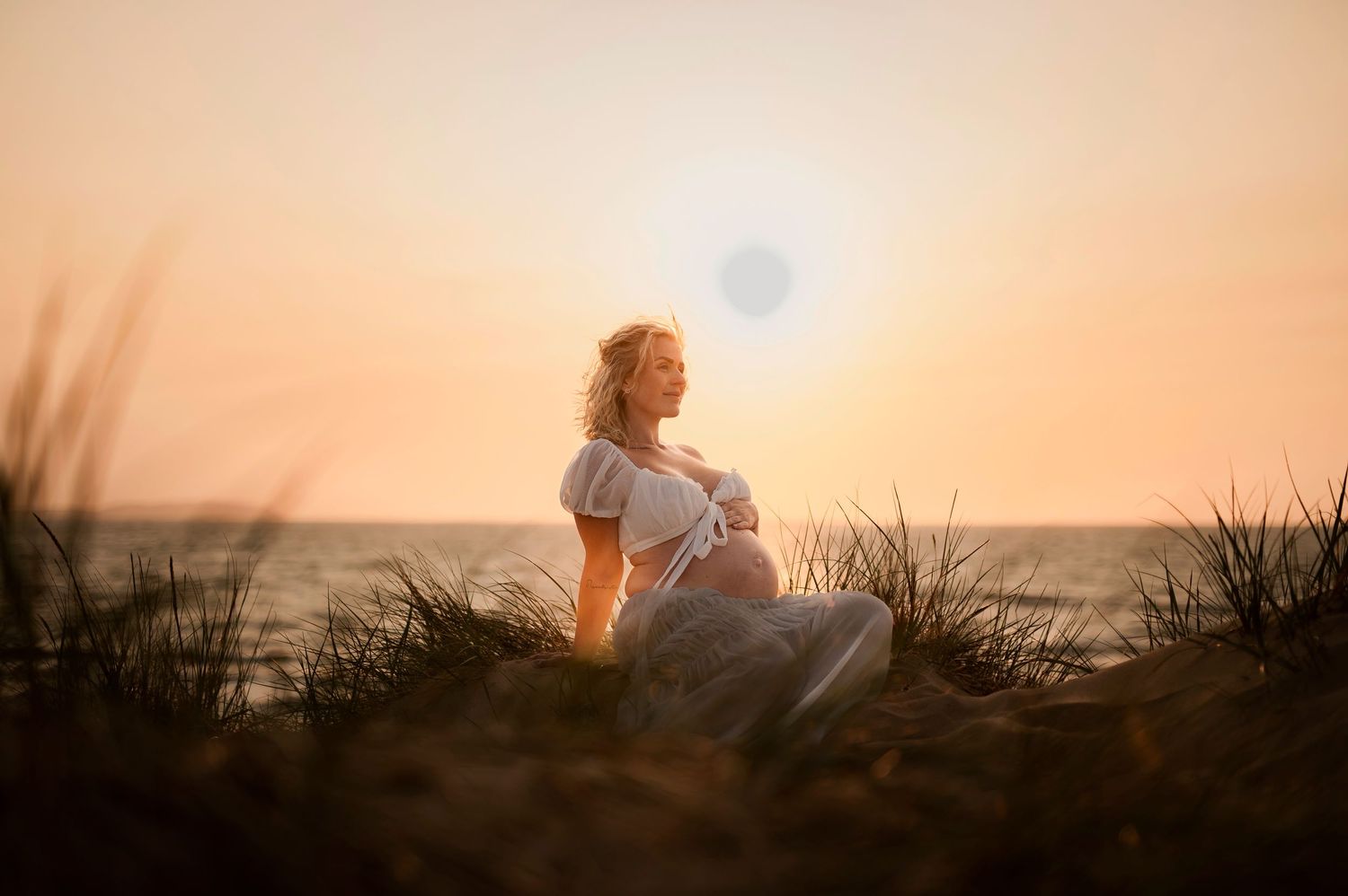 Peaceful sunset maternity portrait on coastal dunes with ocean view.