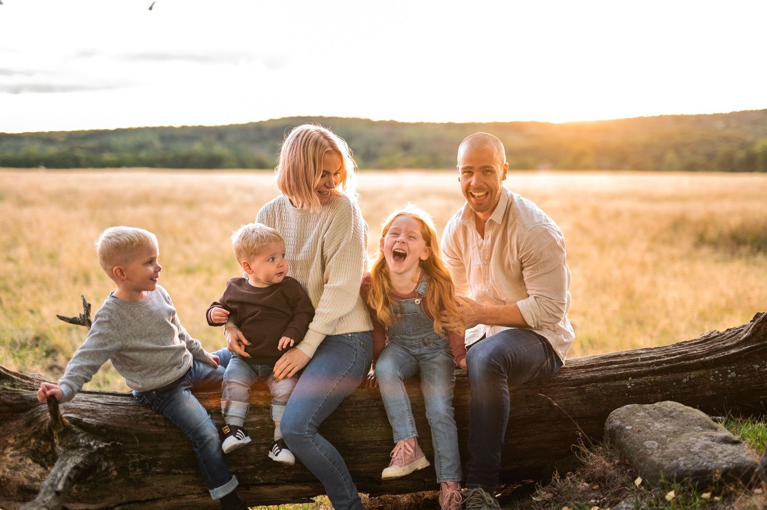 Family enjoying quality time together while sitting on fallen log at sunset.