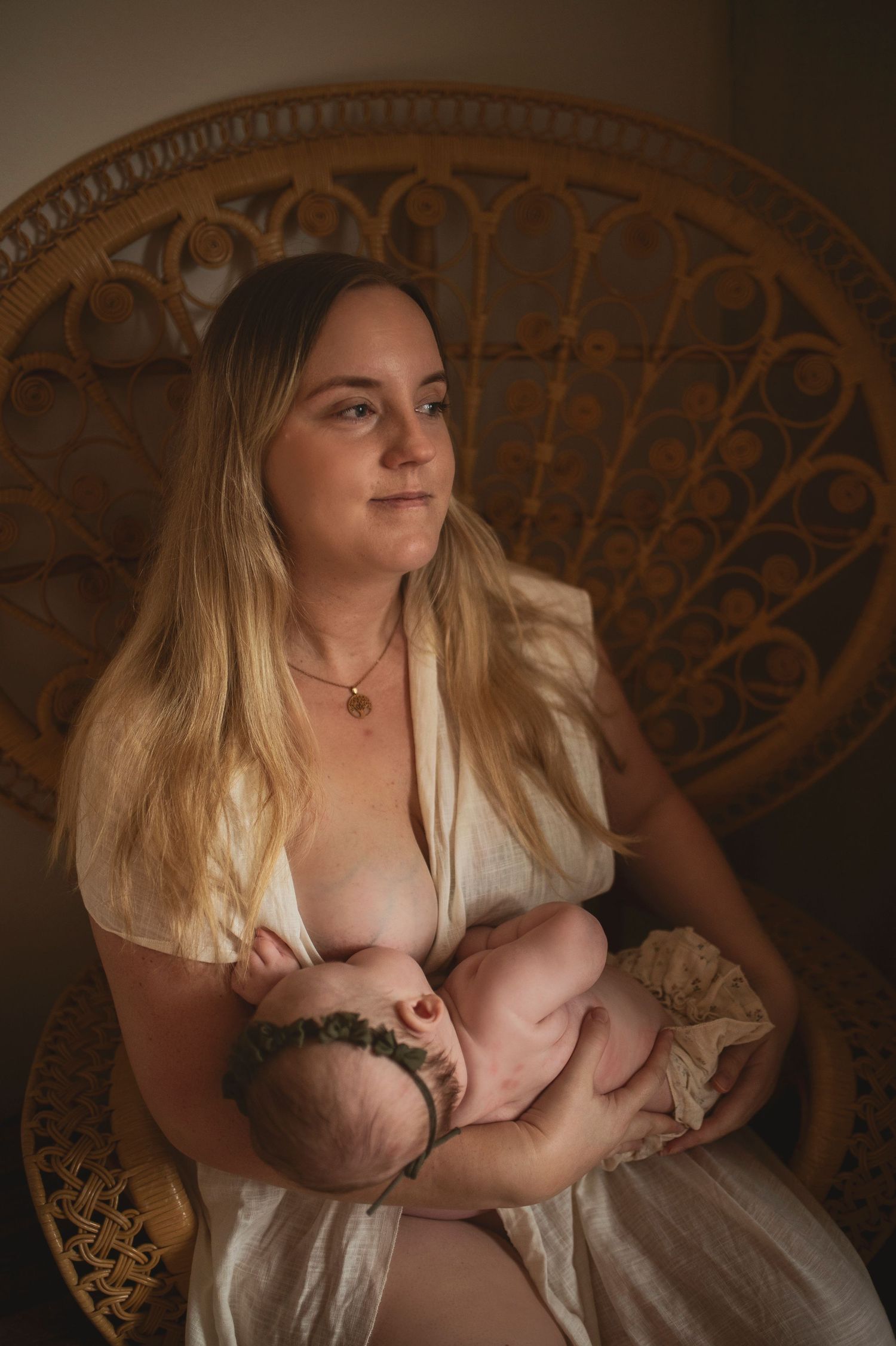 Motherhood portrait in front of wicker chair with warm lighting.