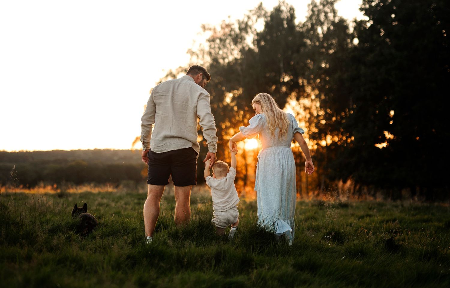 A family stands together in a field during golden hour, silhouetted against the setting sun.