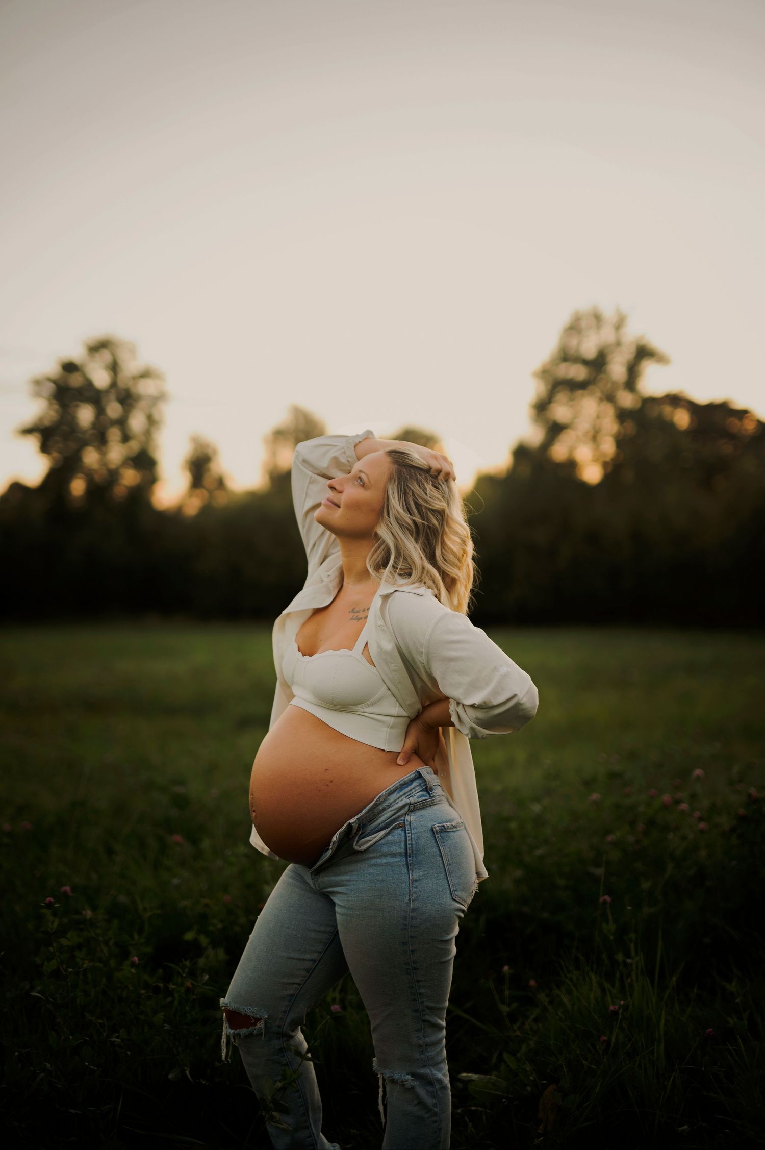 Golden hour maternity photo in a rustic field with dramatic lighting.