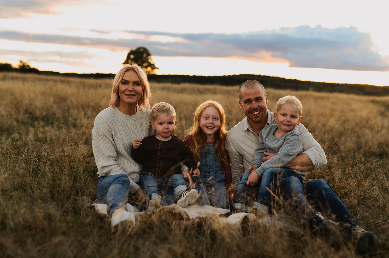 Happy family posing together on blanket in autumn field at sunset.