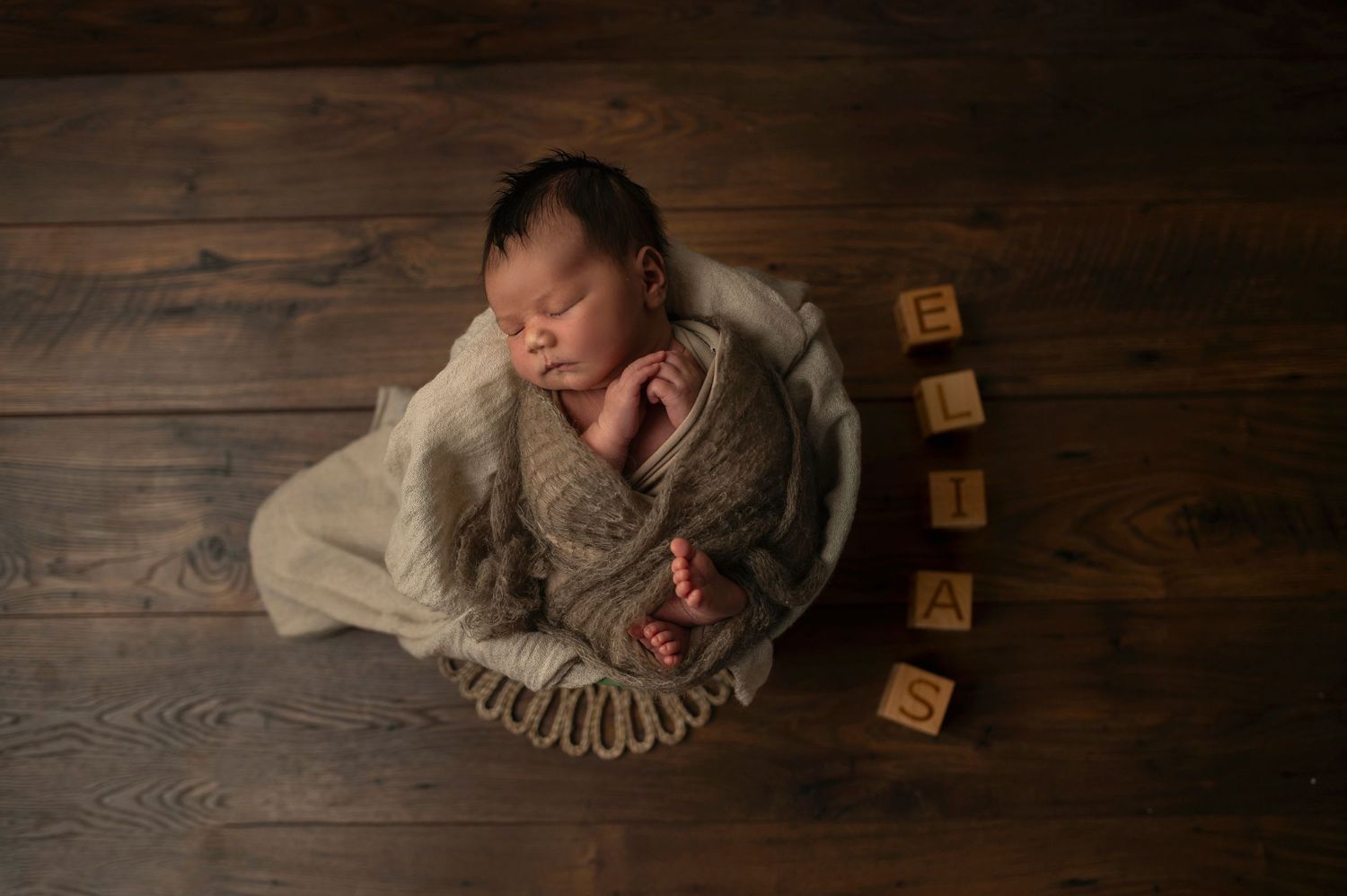 Sleeping newborn in grey wrap photographed from above with wooden alphabet blocks.