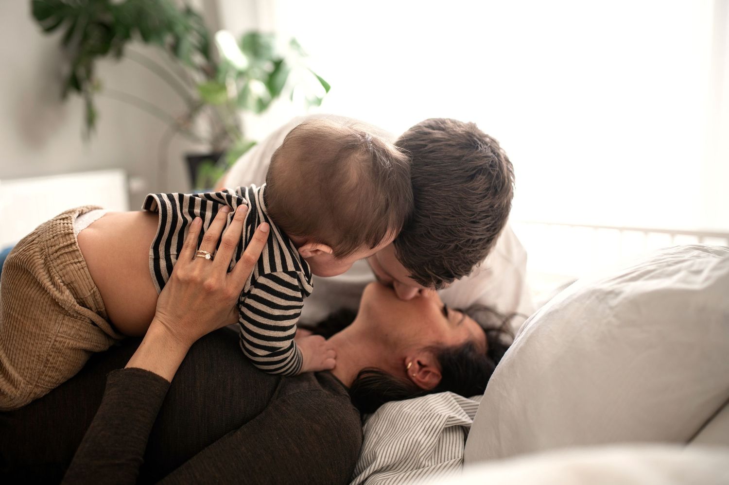 Loving mother lying on couch kissing her smiling baby in a bright living room.