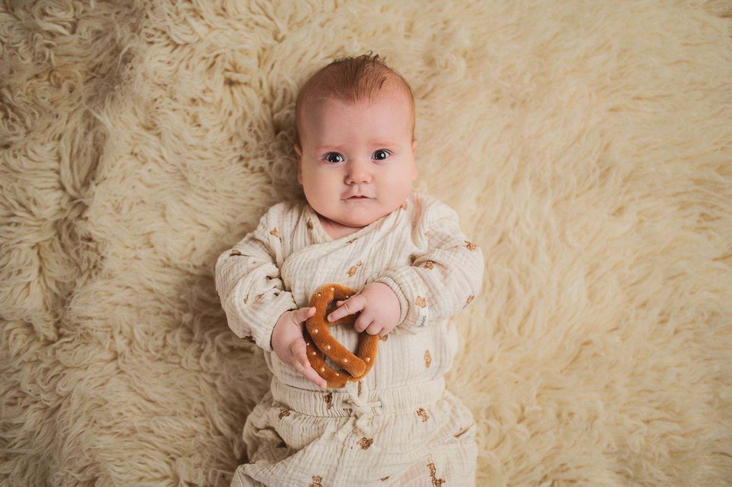 Baby wearing cream-colored outfit lying on fluffy beige rug.
