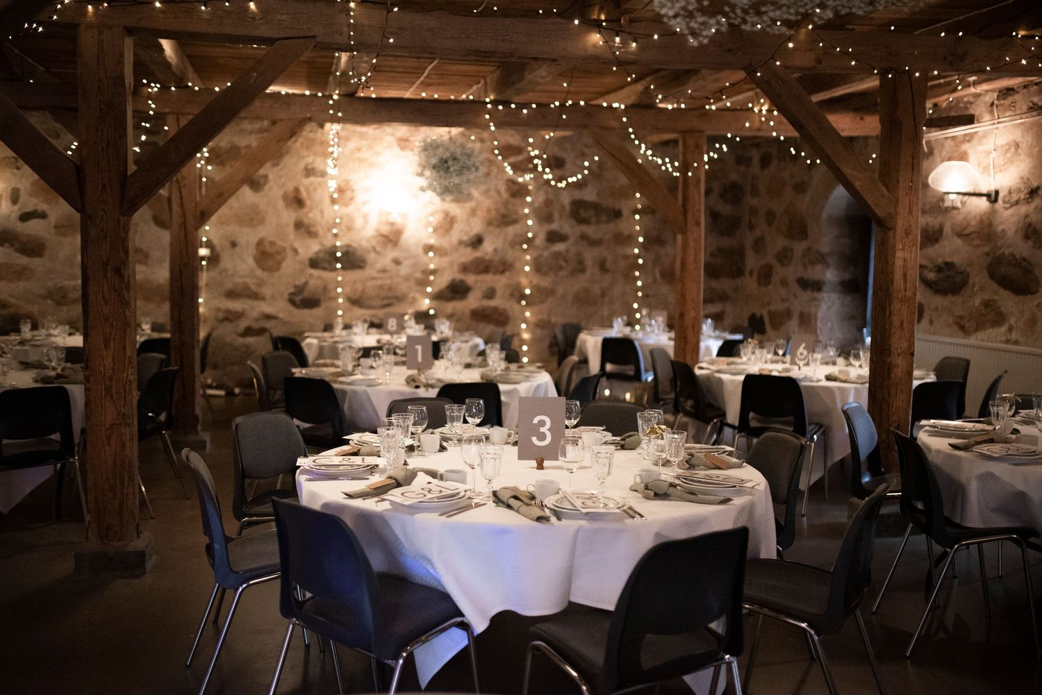 Rustic reception hall with stone walls, wooden beams, and elegant table settings.