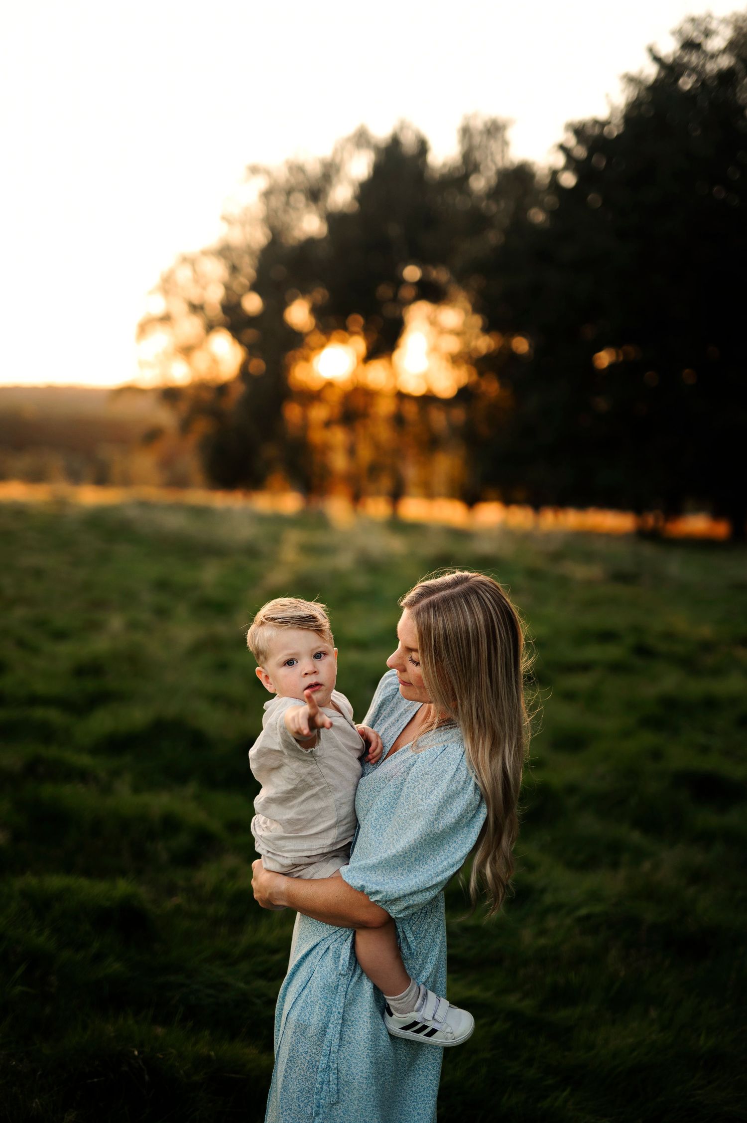 Magical sunset portrait in a green field with trees silhouetted in the background.