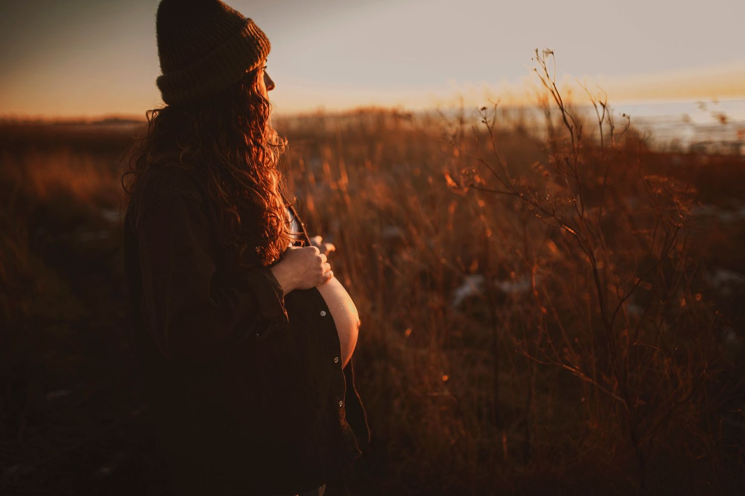 A silhouetted figure in winter attire stands in a golden field at sunset.