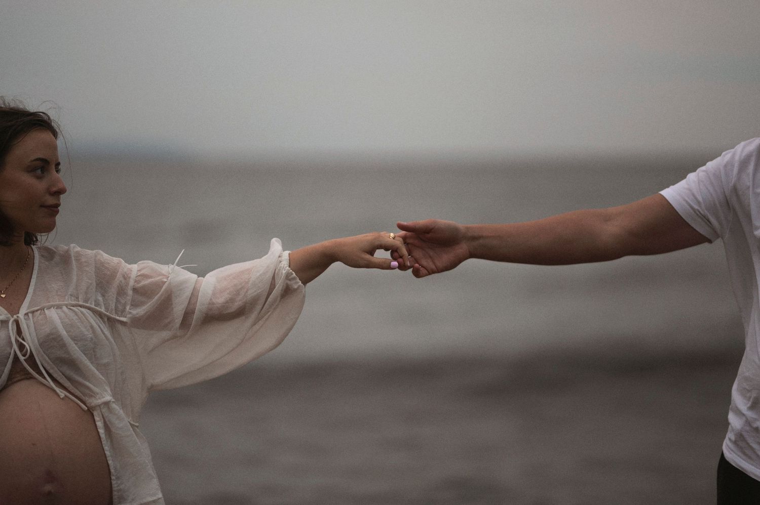 A couple holds hands at sunset during a maternity photoshoot on the beach.