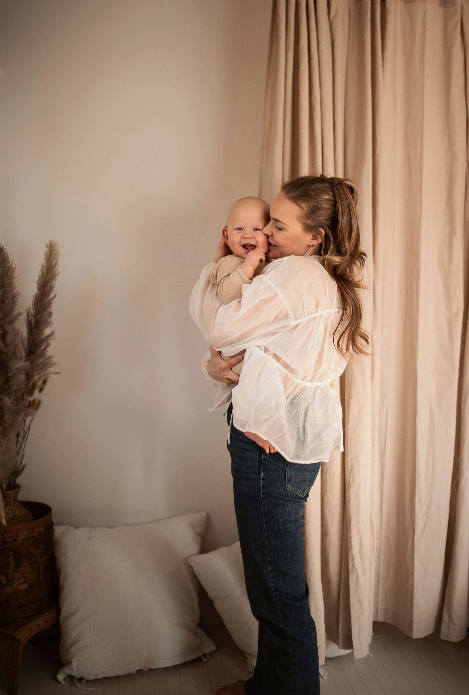 A series of five candid photos showing a tender moment between parent and baby in white and denim against curtained backdrop.