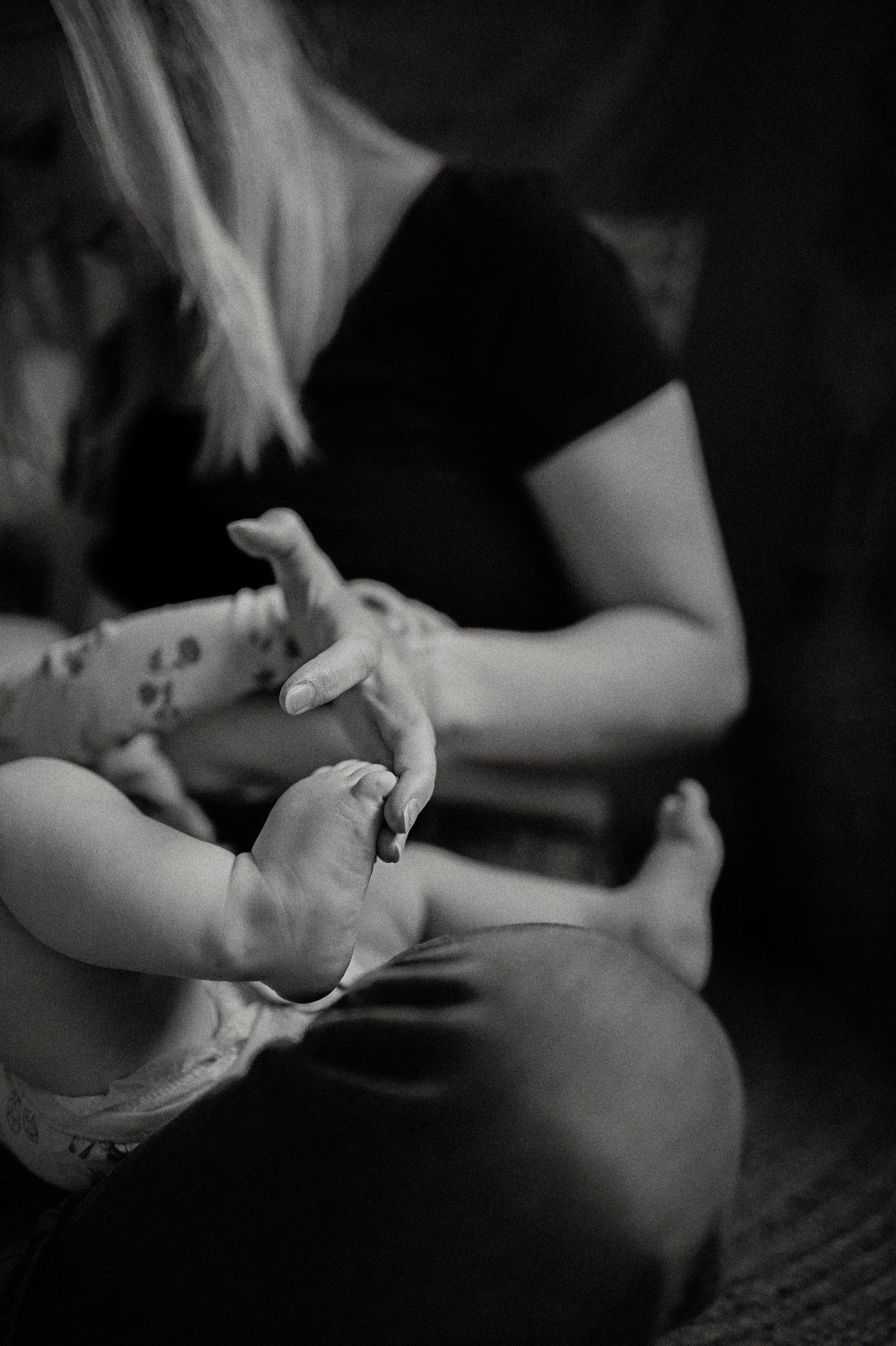 Black and white close-up of tiny baby feet and hands being held gently.