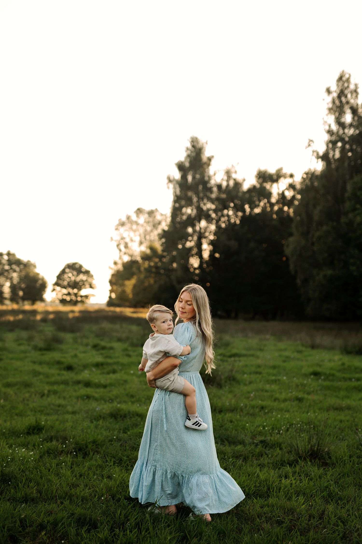 A tender moment captured in golden light as someone holds a small child in a grassy meadow.