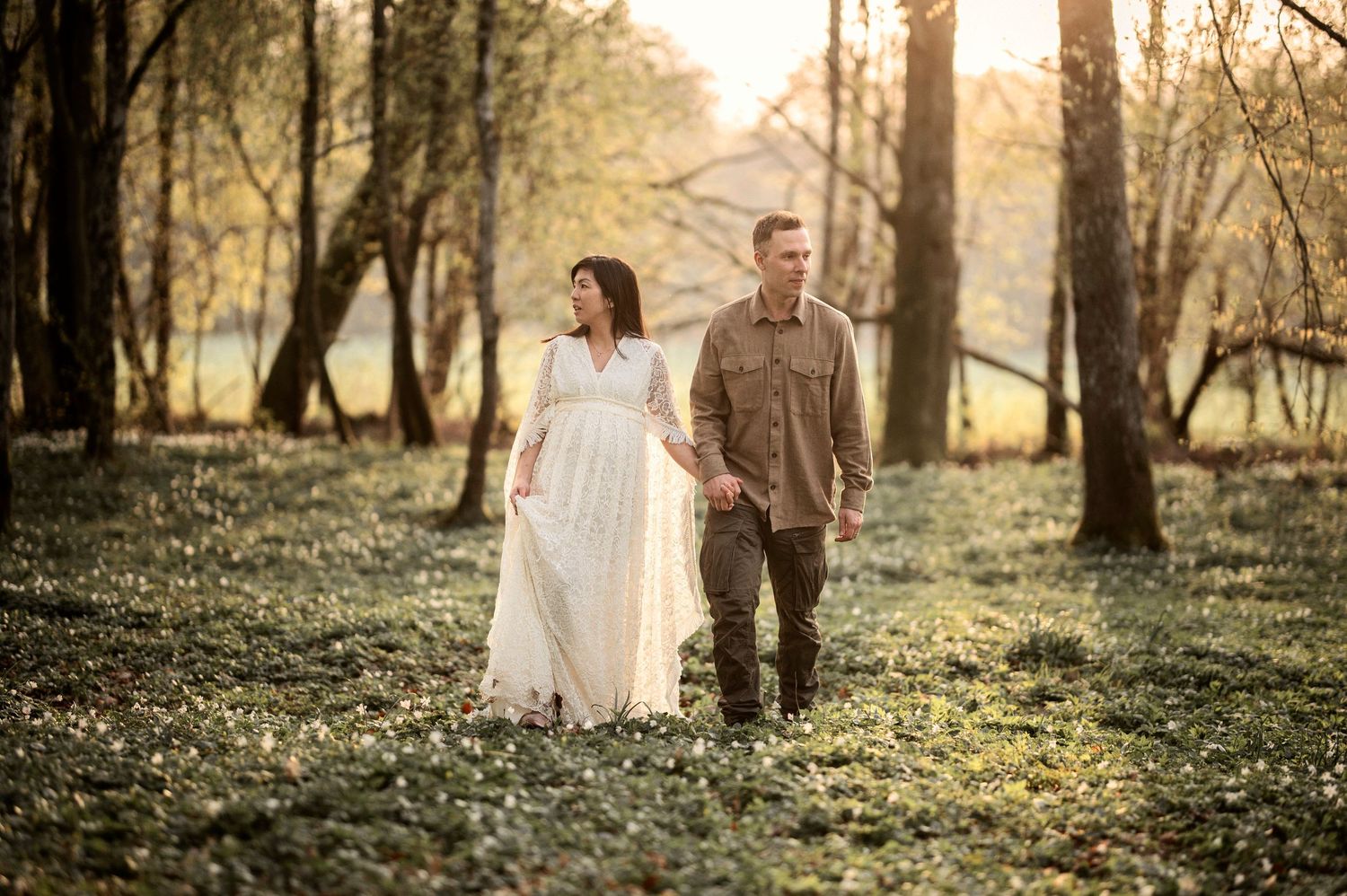 Couple walking together through autumn woods wearing white dress and casual attire.