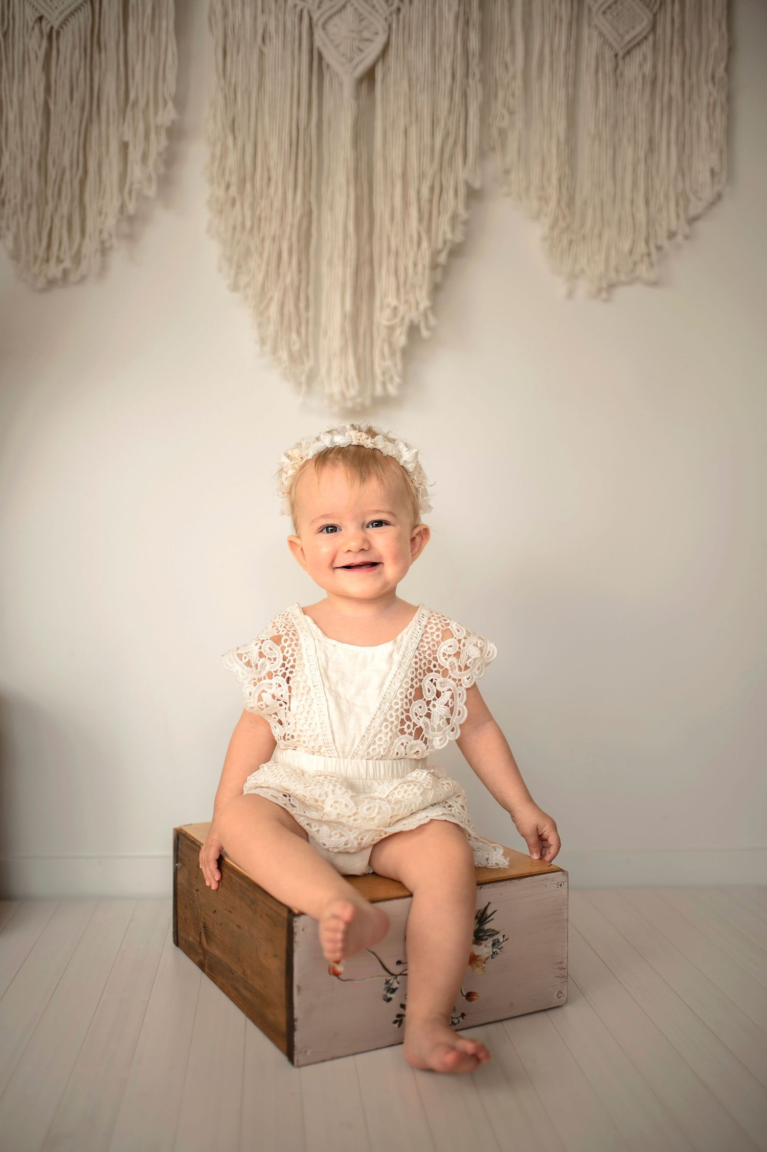 A series of connected images showing a baby in a white lace romper sitting on a wooden box against a neutral background.