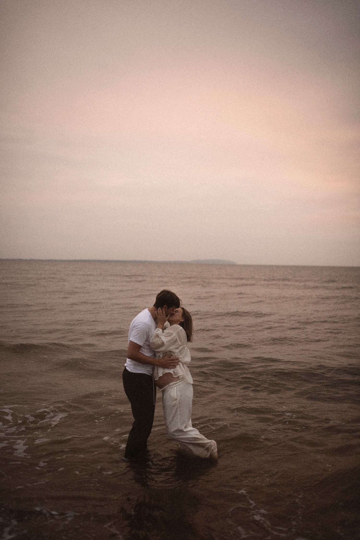 A romantic seaside moment captured as couple embraces in shallow water during sunset.