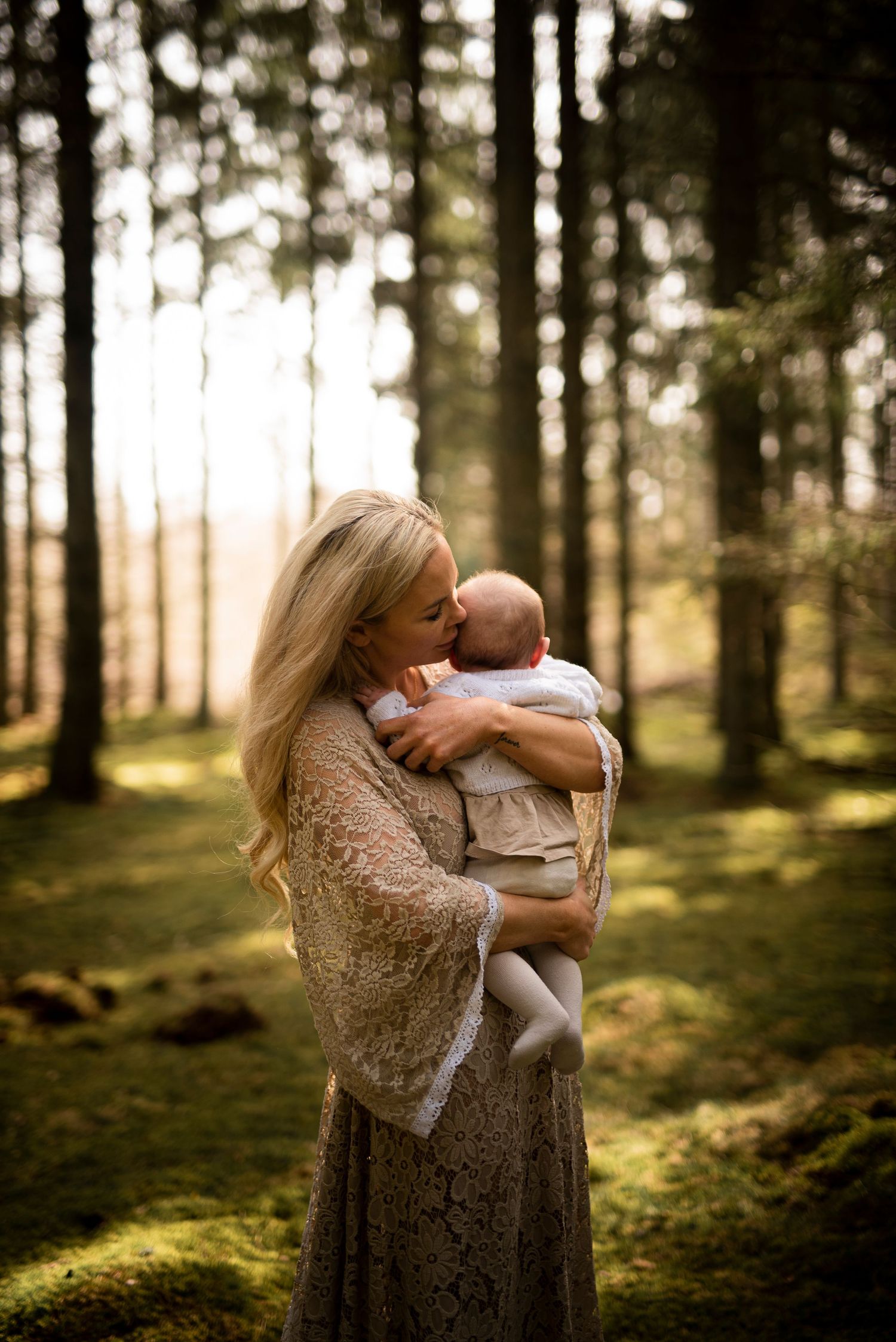 A tender embrace between parent and baby in a sunlit forest with moss-covered ground.