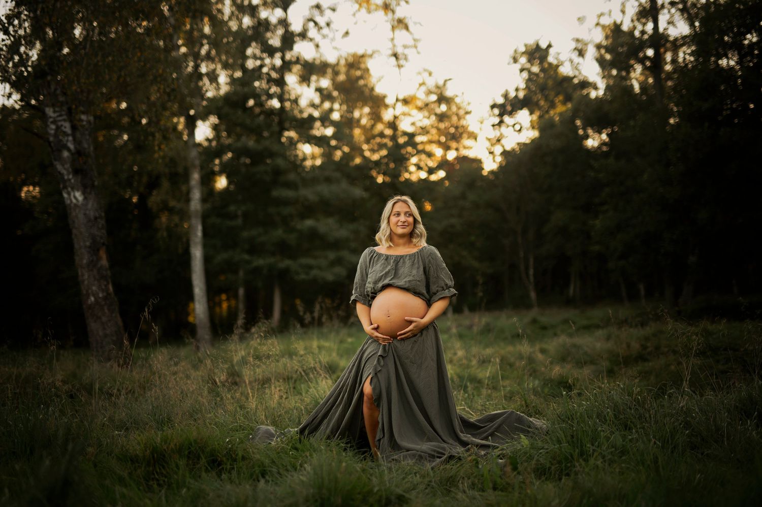 Beautiful outdoor maternity portrait with dramatic lighting and flowing dress in grassy field.