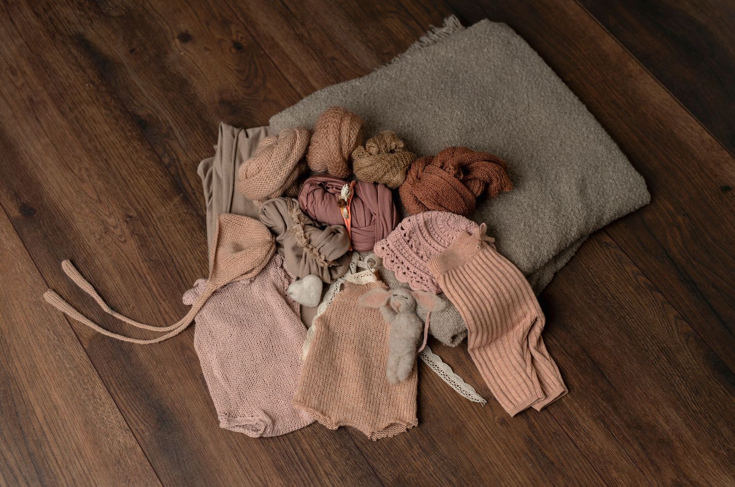 Soft pink and beige baby clothing items arranged on wooden surface.