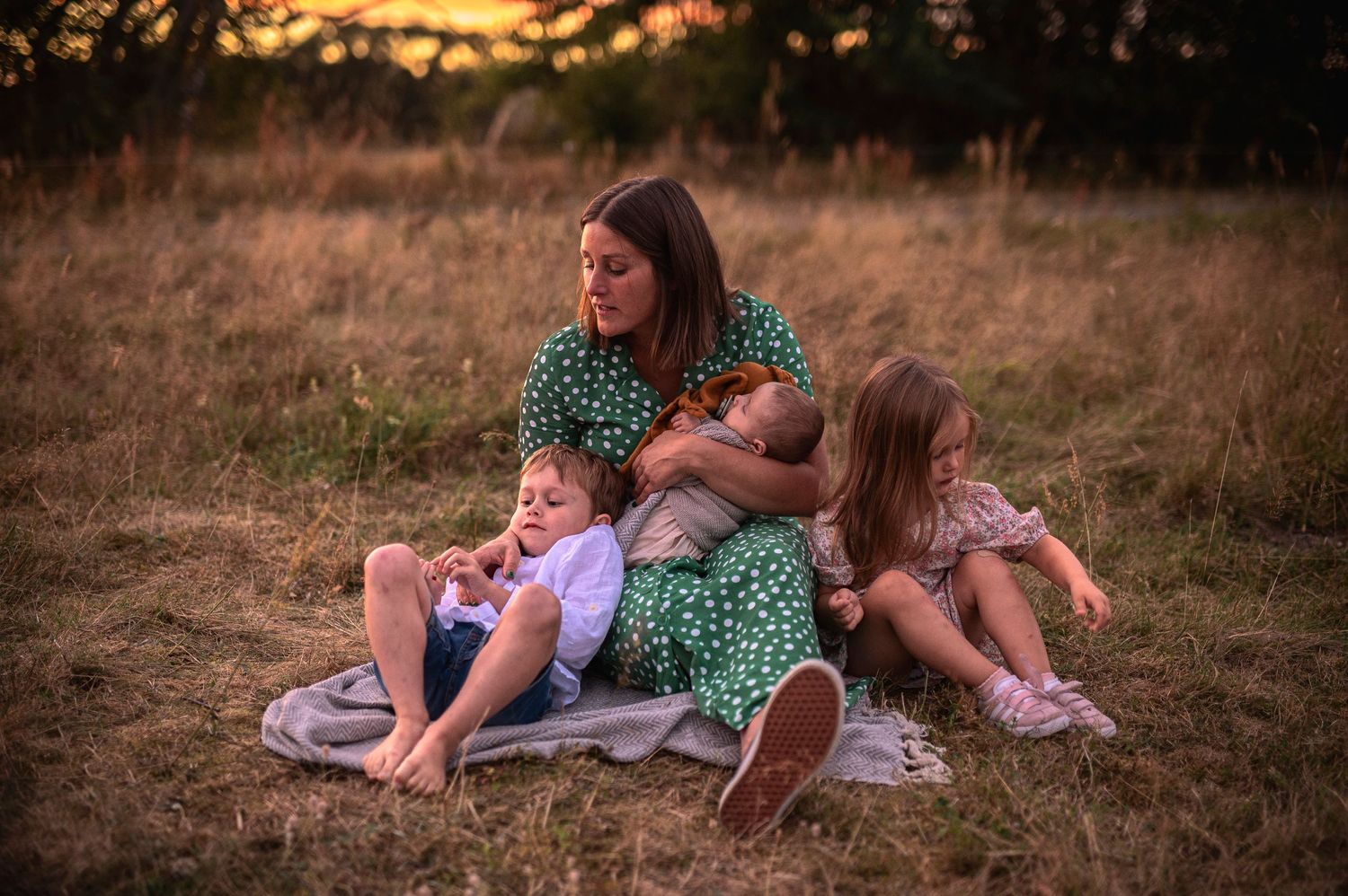 Green polka dot dress-clad group cuddles on blanket in sunlit field.