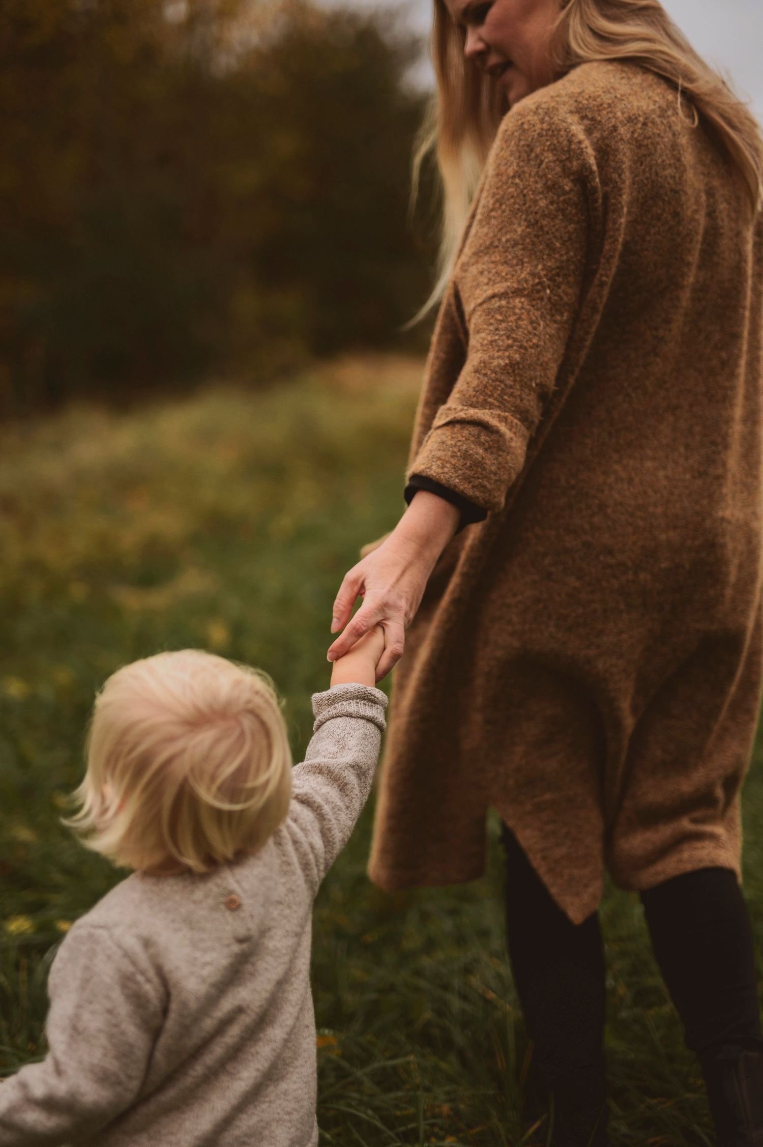 Close-up view of hands joined between adult and child wearing cozy sweaters outdoors.