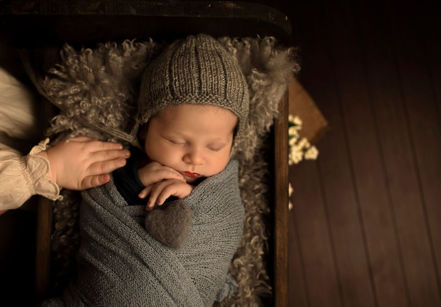 Baby sleeping in gray wrap with knit hat on textured background.
